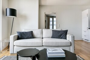 Uma sala de estar moderna com um sofá cinzento, duas mesas de apoio pretas, um abajur e um livro no sofá.