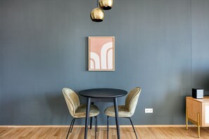 Quarto moderno com parede cinza escura, uma mesa redonda com duas cadeiras e uma obra de arte abstrata emoldurada acima da mesa.