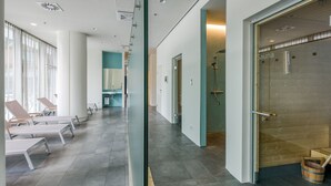 Un espace spa moderne comprenant des chaises longues, un sauna et une salle de douche fermée par des parois de verre.