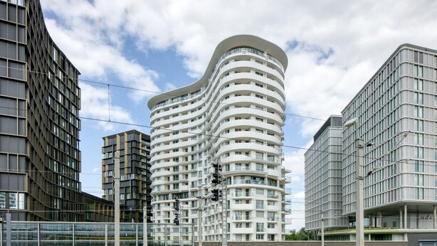 Un immeuble moderne à plusieurs étages, doté d’une façade incurvée, et entouré d’autres constructions contemporaines.