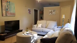 Un salon équipé d’un téléviseur à écran plat, d’un canapé, d’une table basse et décoré avec des œuvres d’art accrochées aux murs.