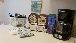 Un comptoir de cuisine avec une machine à café, un ensemble de tasses décoratives, un paquet de capsules de café et une serviette à motifs.