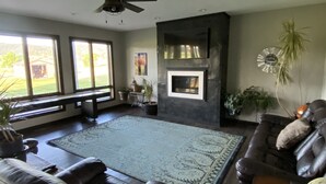 A spacious living room with a fireplace, leather sofas, a large rug, and a view of the outdoors. - All Amenities!  Salt water hot tub!  Walking trail!  In town! (Spearfish)
