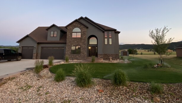 A two-story house with a stone facade, a garage, and a well-maintained lawn. - All Amenities!  Salt water hot tub!  Walking trail!  In town! (Spearfish)
