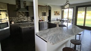 A modern kitchen with a large island, stainless steel appliances, and a dining area with a view. - All Amenities!  Salt water hot tub!  Walking trail!  In town! (Spearfish)