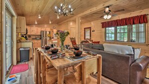 L’intérieur chaleureux d’un chalet comprend un coin repas, des meubles en bois, un ventilateur de plafond et une grande fenêtre avec des rideaux.