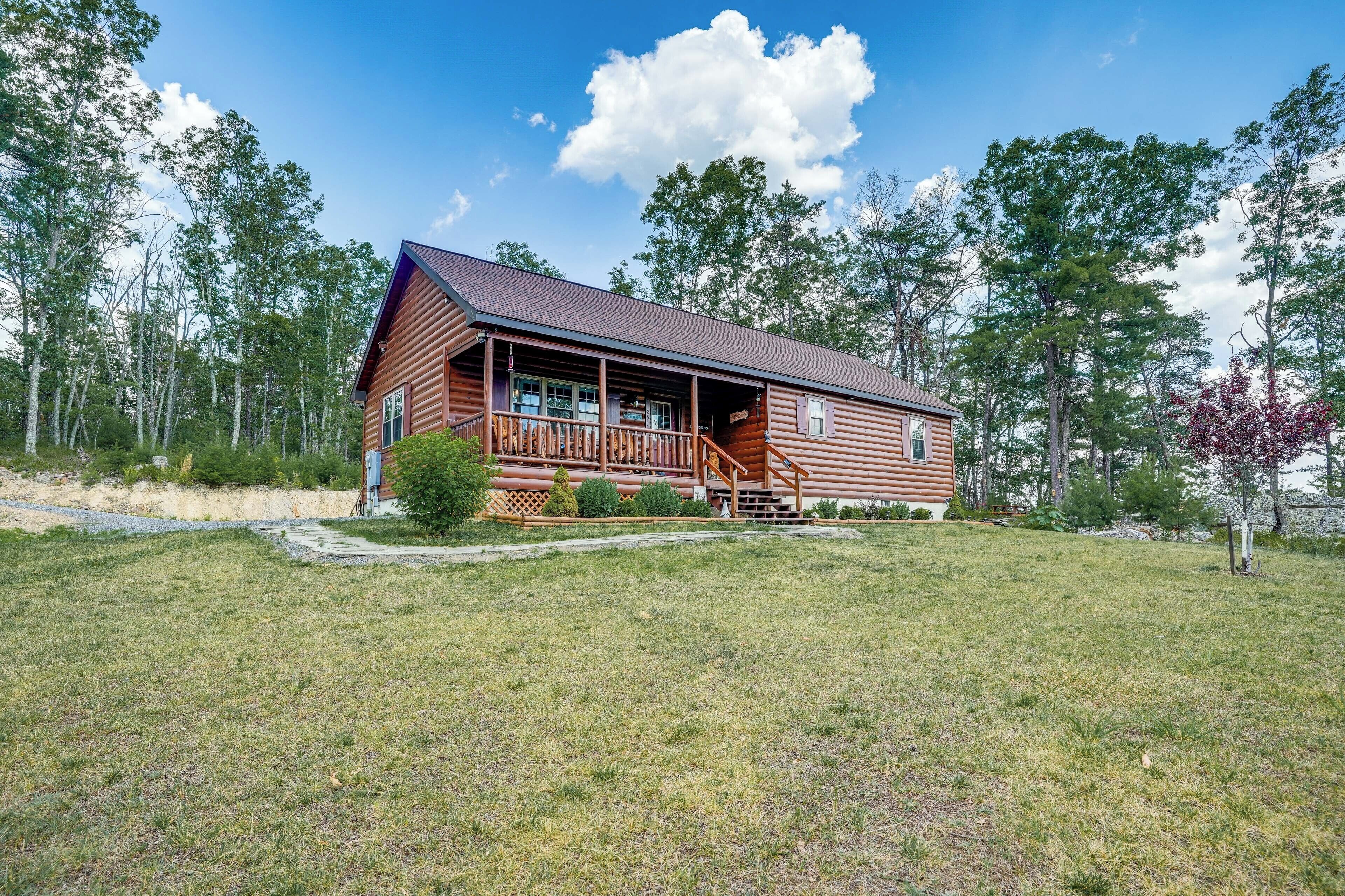 A log cabin with a porch and steps leading to the entrance, surrounded by a grassy yard and trees.