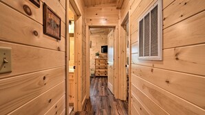 Un couloir intérieur aux murs en bois, avec un plancher en bois, une grille d’aération sur le mur de droite et un tableau encadré sur le mur de gauche.