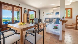 Ein Essbereich mit Tisch und Stühlen, einer Couch und einem Fernseher. Fenster bieten Meerblick.