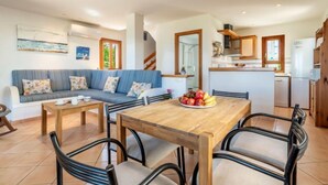 Ein modernes Wohnzimmer mit einer Couch, einem Holzespeisetisch mit Stühlen und einer Küchenzeile inklusive Kühlschrank und Schränken.