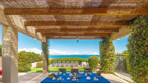 Ein überdachter Essbereich im Freien mit Tisch für vier Personen, mit Blick auf einen Pool und das Meer.