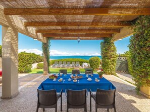 A covered outdoor dining area with a table set for four, overlooking a pool and the sea. - Ran de Mar 35 by Interhome (Colònia Sant Pere)