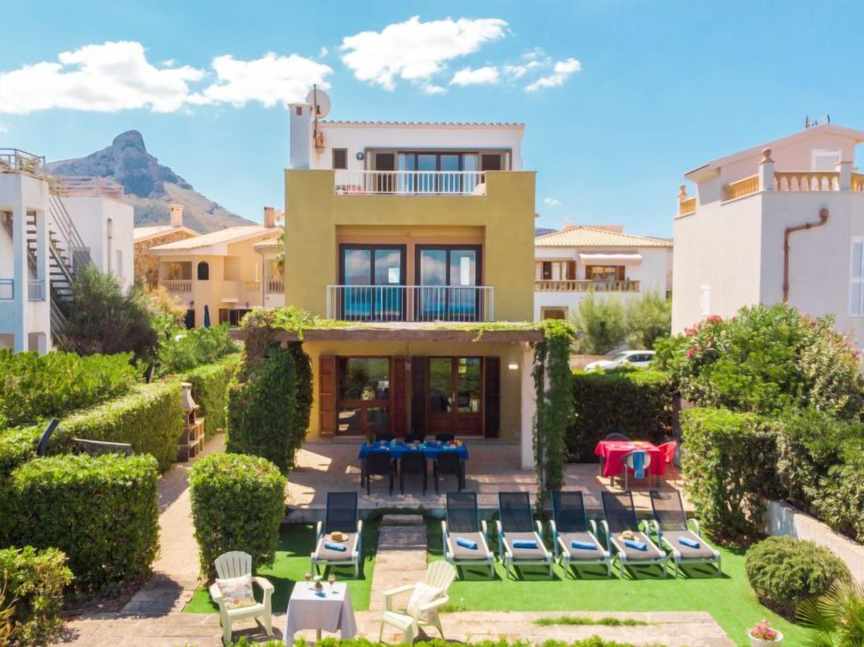 A two-story building with a balcony, surrounded by well-maintained gardens and a pool area with lounge chairs.