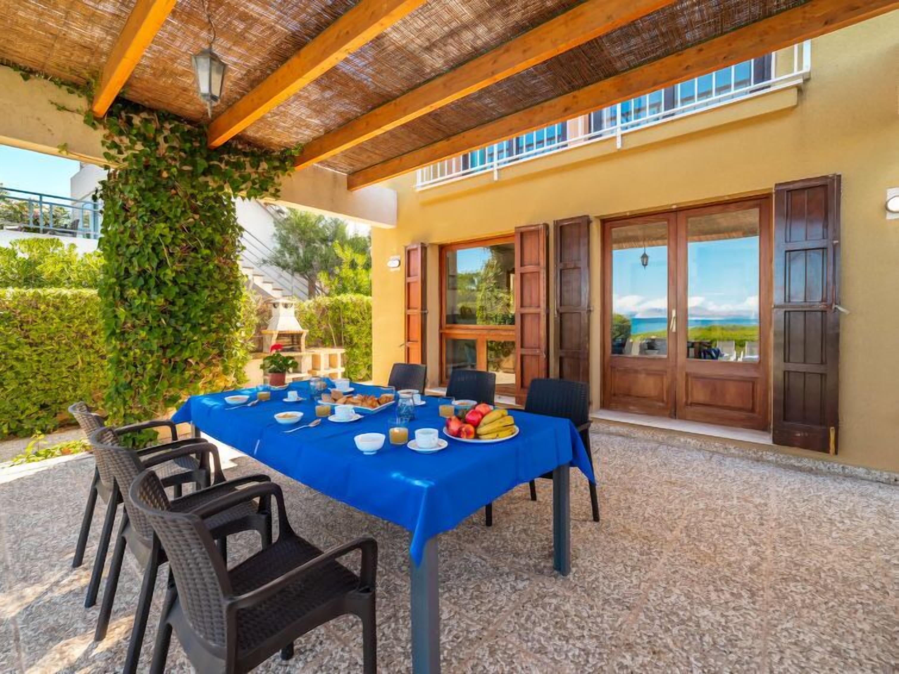 An outdoor dining area with a blue tablecloth, chairs, and a view of the sea.