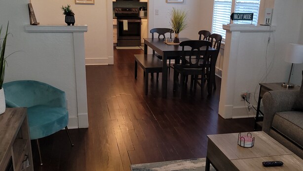 A modern living room with a dining area, wooden flooring, and a kitchen in the background. - Pensacola Breeze/ Downtown (Pensacola)