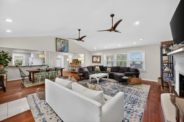 A spacious living room with a sectional sofa, a dining area with a table and chairs, ceiling fans, and a fireplace.