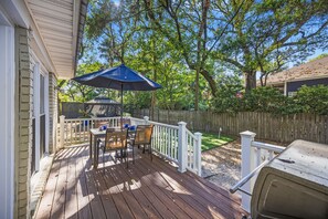 A wooden deck with a table and chairs, a barbecue grill, and a blue umbrella.