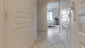 Ein Flur, der in ein Schlafzimmer mit Bett, Schreibtisch und Fernseher führt.