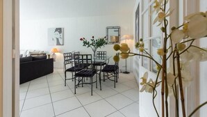 Ein Essbereich mit Tisch und Stühlen, einer Vase mit Blumen und einer Couch im Hintergrund.