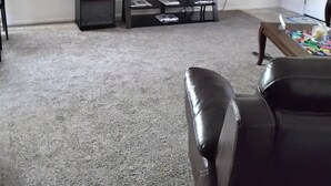 Olohuoneessa on tasainen näyttö, joka on asennettu jalustalle, seinäkello ja kattotuuletin.
