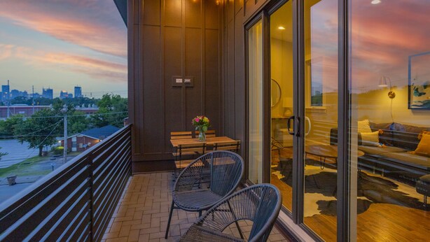 Un balcón con vista a la ciudad, una mesa con sillas y un sofá dentro de una habitación con puertas de vidrio.