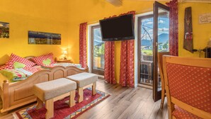 Una habitación con cama, banco, televisor y ventana con cortinas.