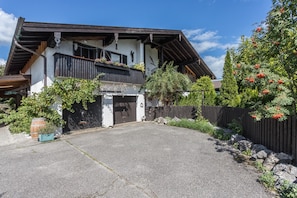 A traditional chalet with a wooden balcony, a garage entrance, and a stone pathway leading to the door.