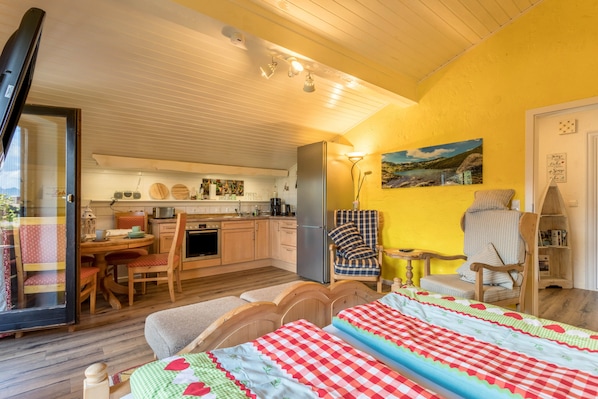 A cozy room with a bed, a chair, a small table, and a kitchen area.