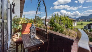 Un balcón con una mesa de madera, un farol y vistas a un jardín y casas.