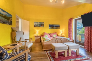 A room with a bed, a chair, a bench, a small table, and a TV.