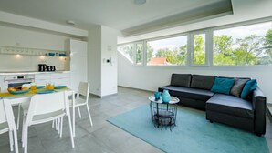 Un soggiorno moderno con cucina, zona pranzo e un'ampia finestra vista alberi.
