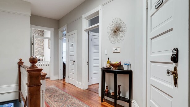 A hallway with white doors, a wooden staircase, and a patterned rug. - Carytown Gem | Spacious Family-Friendly Apartment (Richmond)