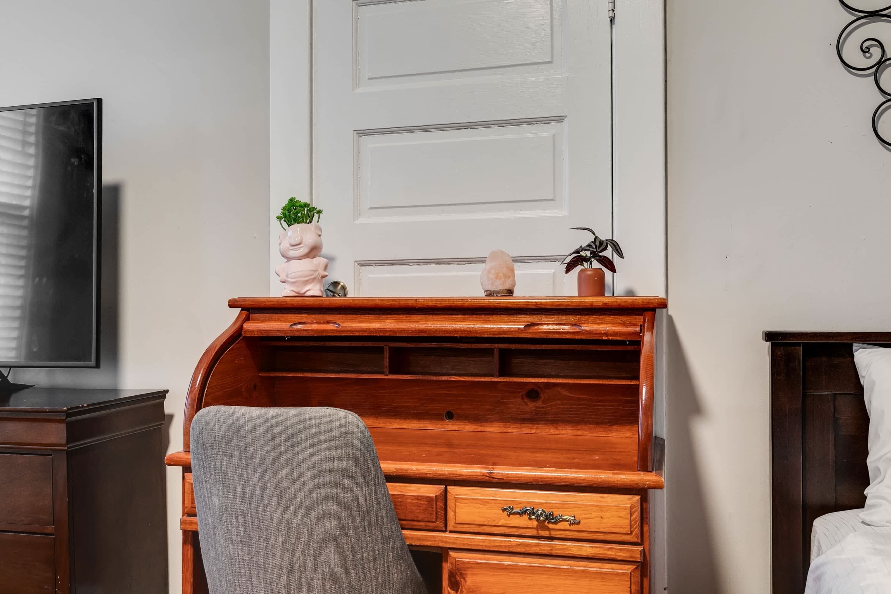 A room with a wooden desk, a chair, a television, and a bed.