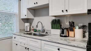 A kitchen with white cabinets, a marble countertop, a sink, and various kitchen appliances. - Carytown Gem | Spacious Family-Friendly Apartment (Richmond)