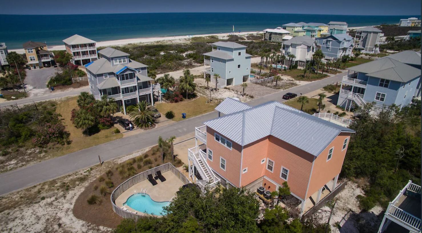Zona residencial costera con casas, una piscina y una playa al fondo.