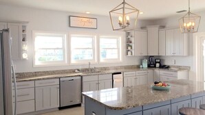 A modern kitchen with white cabinets, granite countertops, and a central island with stools. There are pendant lights above the island and a coffee machine on the countertop. - Dates Available!!  Check out our property!! (Port St Joe)
