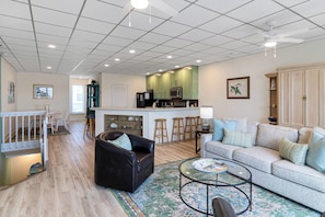 A spacious living room with a sofa, a coffee table, and a dining area with chairs and a small kitchen in the background.
