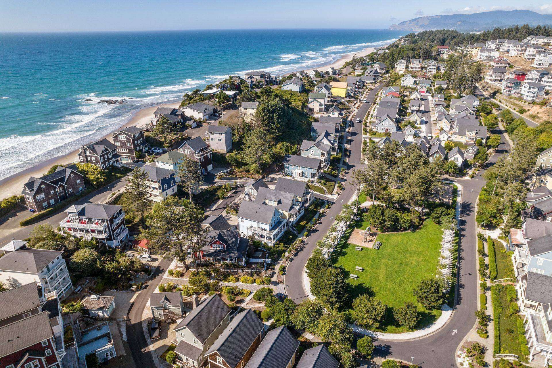 An aerial view of a coastal residential area with houses, a beach, and a road.