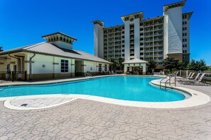 A swimming pool with a hexagonal tiled deck, surrounded by lounge chairs and a building with multiple balconies.
