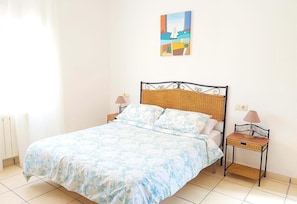 Un lit recouvert d’une couvre-lit à motifs floraux, deux tables de chevet avec des lampes, une tête de lit en osier et un tableau au-dessus du lit.