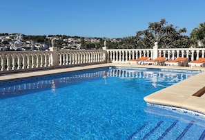 Une piscine aux eaux cristallines, bordée de carreaux, avec une balustrade blanche et des chaises longues orange.