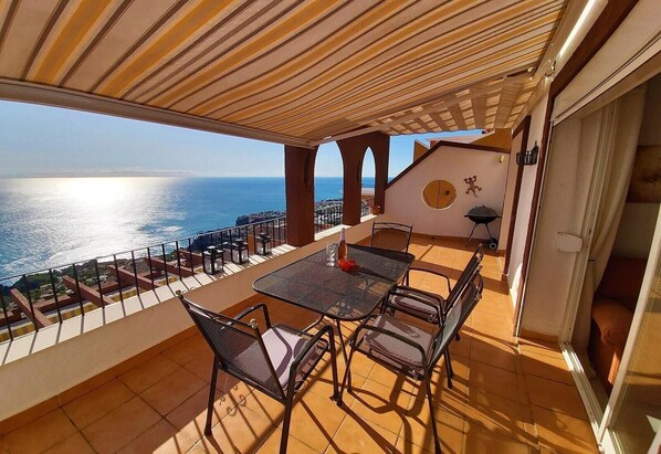 A terrace with a table and chairs, a view of the sea, and a barbecue grill.
