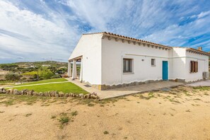 A white building with a blue door, a stone wall, and a grassy area in front.