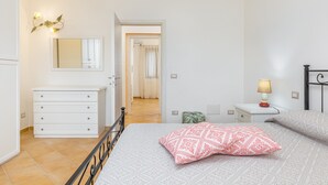 Et soveværelse med seng, kommode, natbord med lampe, spejl og en dør til et andet rum.