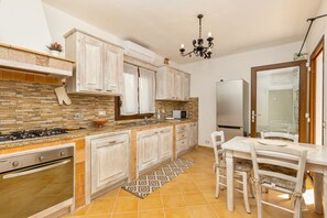 A kitchen with a stone backsplash, white cabinets, a gas stove, and a dining area with a table and chairs.