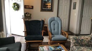 A living room with two armchairs, a coffee table with magazines, a floral sofa, and a door with a wreath. - Bright and cheerful. With glorious sunrise/sunset views, close to Glacier park. (Columbia Falls)