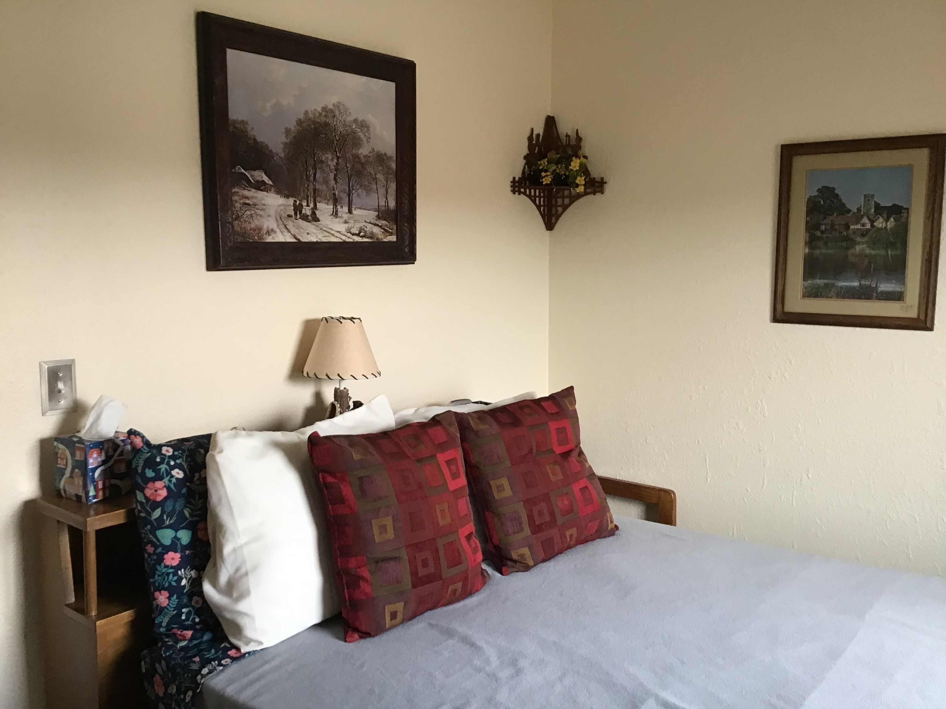 A bedroom with a bed, pillows, a nightstand, a lamp, and two framed pictures on the wall.