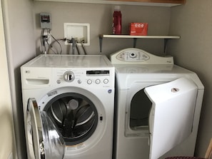 A laundry area with two washing machines, a control panel, and a shelf with a bottle and a box.