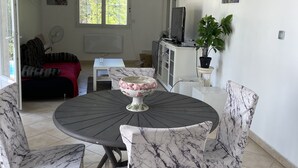 Een eetruimte met een ronde tafel, vier stoelen met marmeren bekleding, een decoratieve schaal en een televisie op een kast.