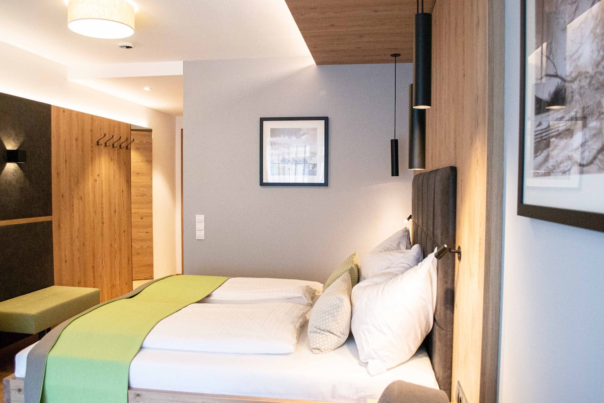 A hotel room with a bed, a bench, a framed picture on the wall, and a wooden panel on the left.